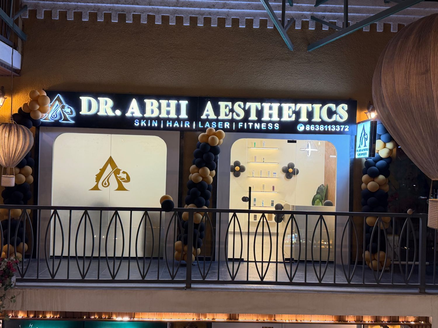 The illuminated Dr. Abhi Aesthetics shopfront at night, its gold sign reading Skin, Hair, Laser, Fitness.