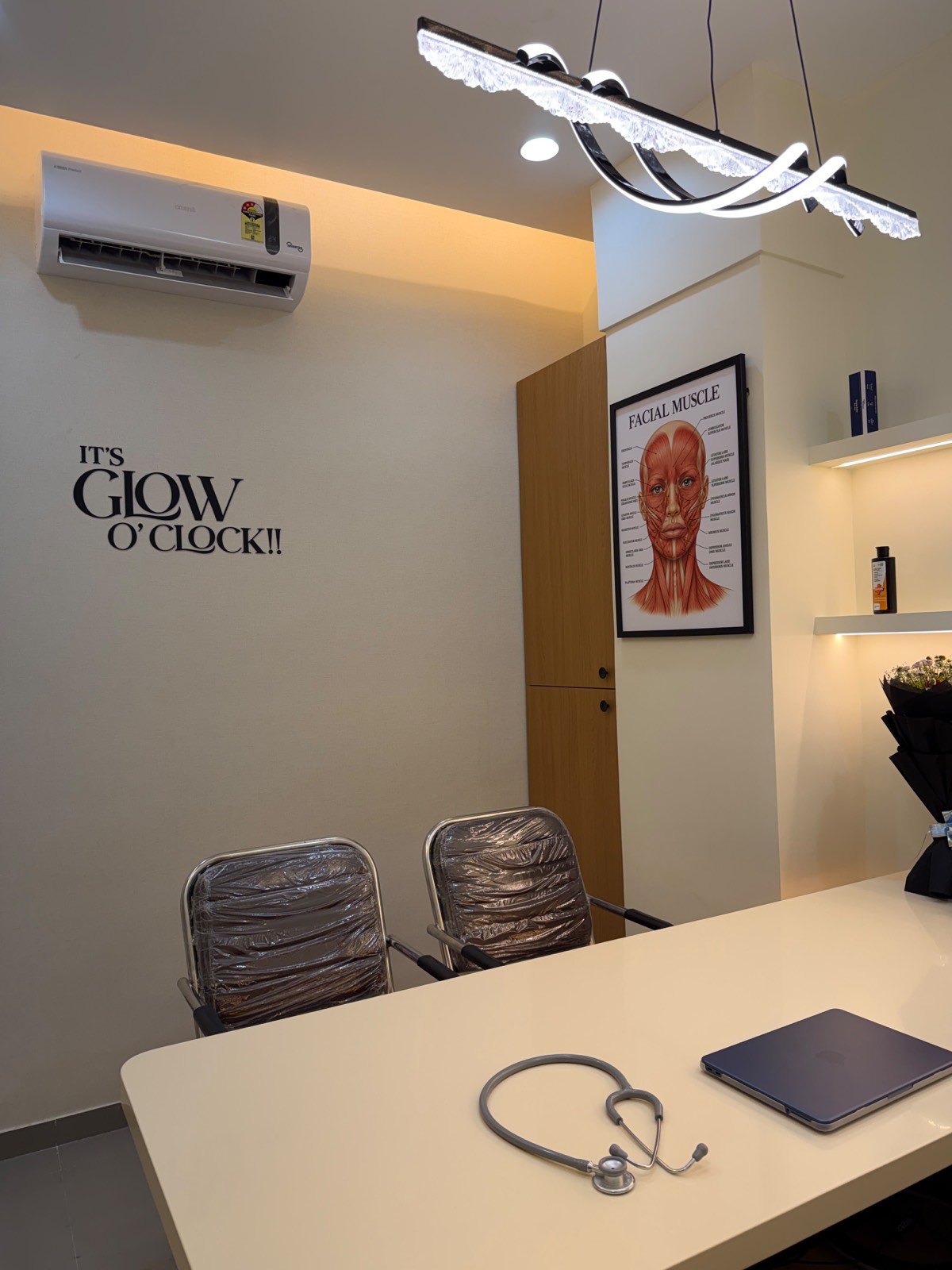 The consulting room at Dr. Abhi Aesthetics, with a desk, patient chairs and a facial anatomy chart.